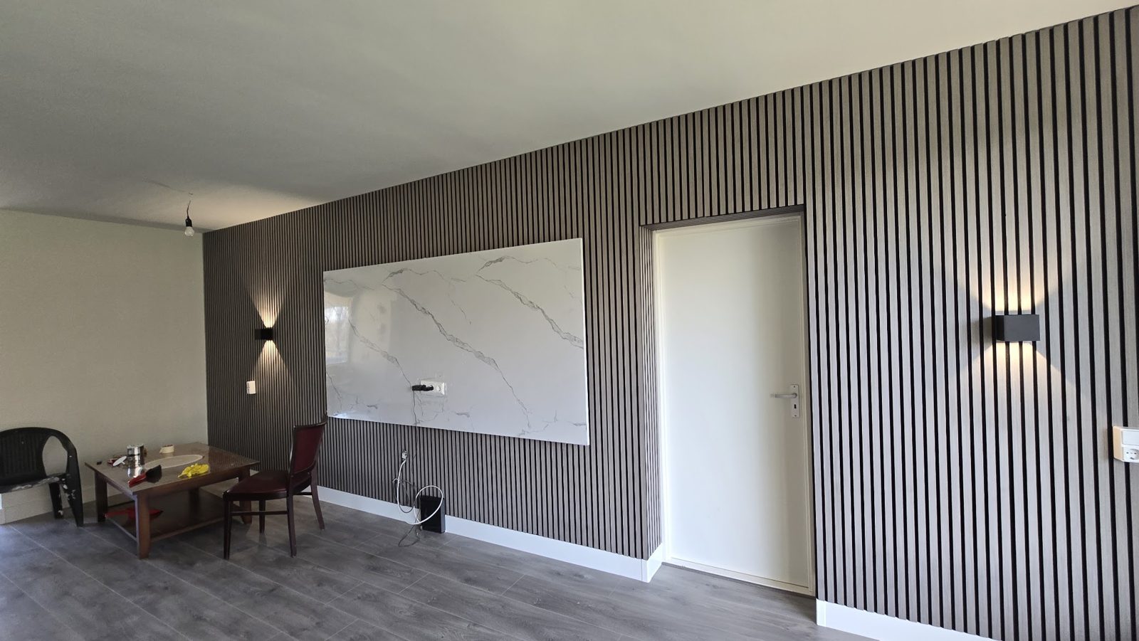 Donkere lamellenwand met een wit paneel in marmerlook en wandlampen