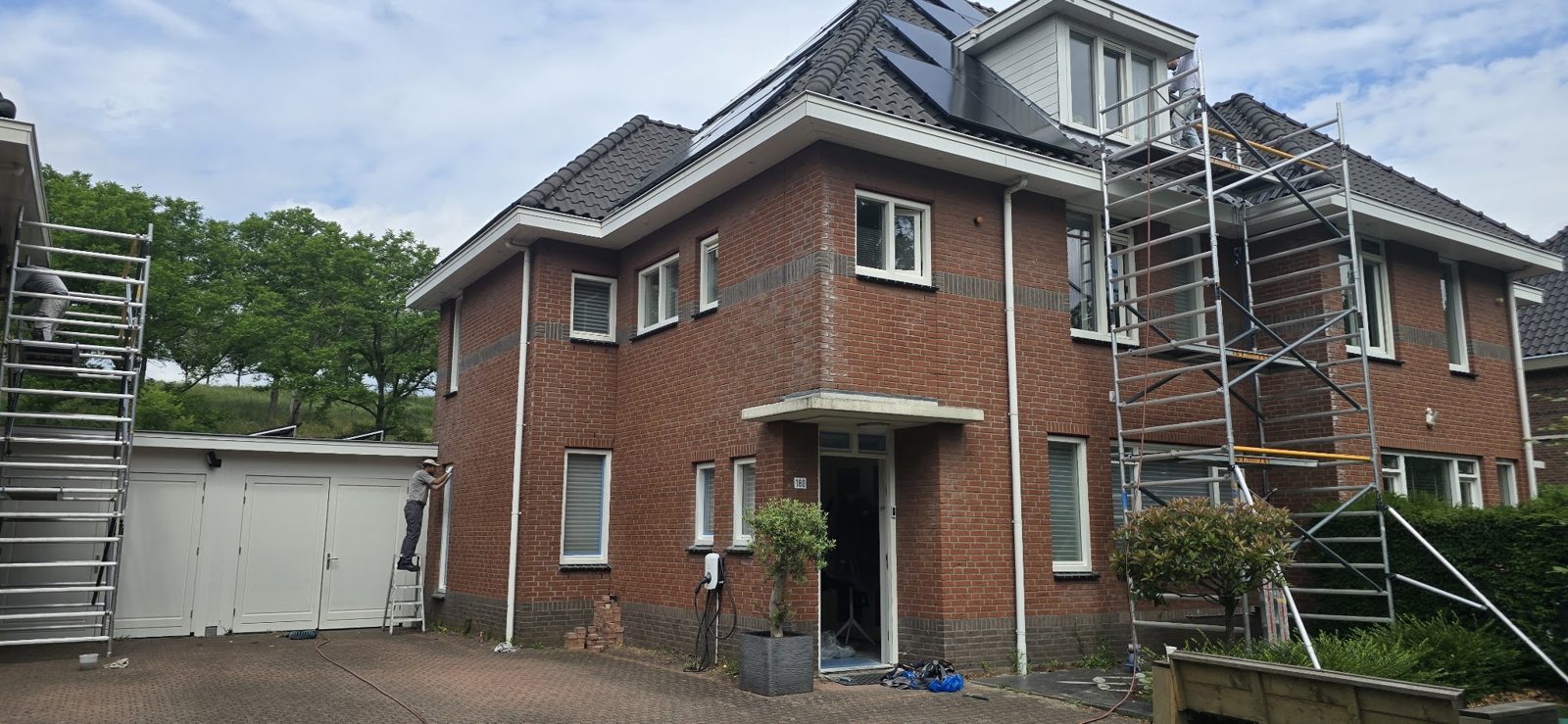 Vrijstaande bakstenen woning met rolsteigers en een vakman op een ladder bij de garage