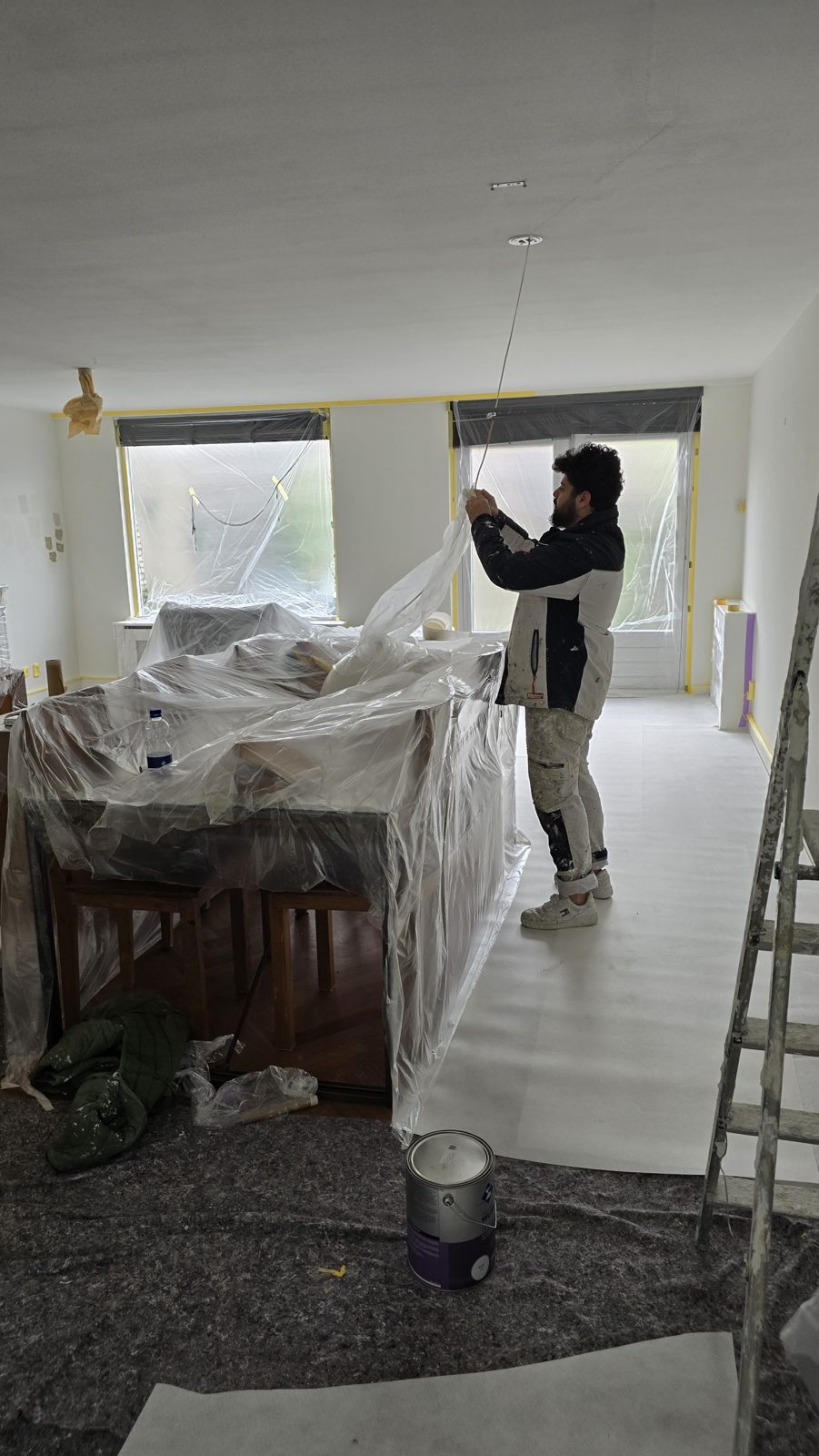 Schilder dekt de eettafel af met plastic voordat het schilderwerk begint